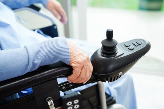 Asian elderly woman disability patient sitting on electric wheelchair in park, medical concept.