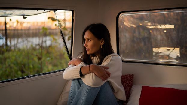 Pensive Caucasian woman in light sweater motorhome in warm autumn. Travel in a van