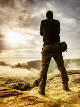 Photographer bend head check display of camera. Man stay on cliff and takes photos. Autumn beautiful misty landscape misty sunrise at horizon