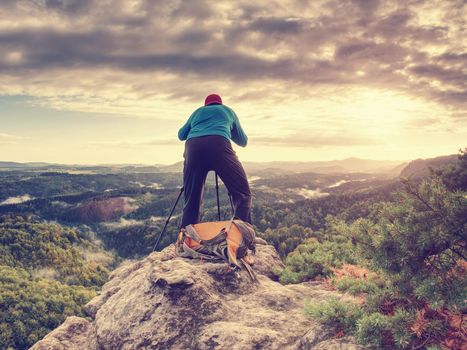 Freelancer create nature photos. Professional photographer takes photos with camera on tripod on rocky peak. Dreamy fogy landscape