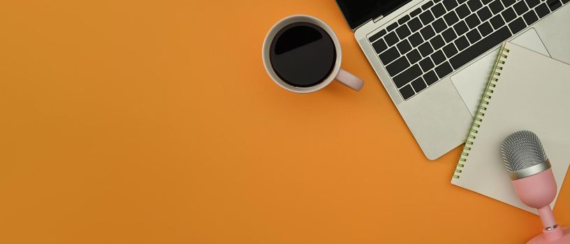 Flat lay laptop, coffee cup, notepad and microphone for podcasts on pink background. Copy space for your text.