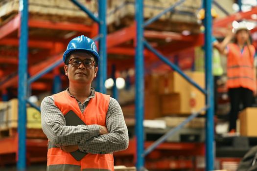 Portrait of mature male supervisor standing in warehouse with his arm crossed and looking at camera.