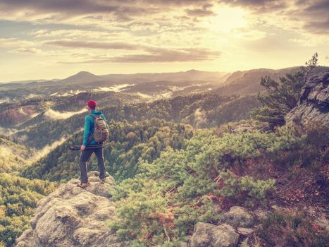 Freelancer create nature photos. Professional photographer takes photos with camera on tripod on rocky peak. Dreamy fogy landscape