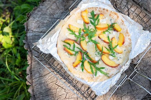 Very tasty and interesting pizza with peach and dor blue with arugula. Delicious, interesting taste of fruit pizza. Grilled pizza, outdoor recreation