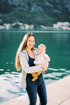 Smiling mom with a baby in her arms stands on the pier. High quality photo