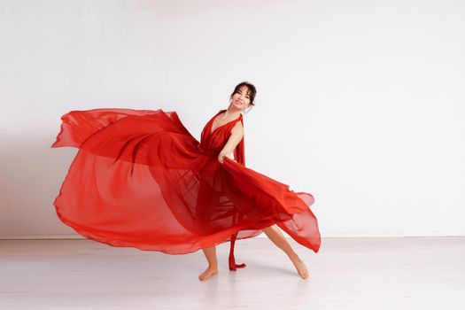 Dancer in a red flying dress. Woman ballerina dancing on a white studio background.