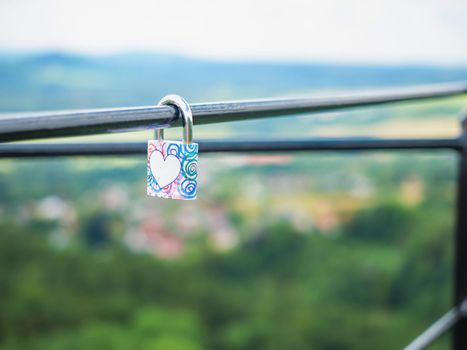 Locked lock hangs on the metal fence. Symbol of love in the park. The metal red lock in the shape of a heart is locked with a key