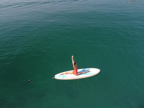 Young attractive brunette woman in red swimsuit, swimming on kayak around volcanic rocks, like in Iceland. Back view. Christmas holiday vacation and travel concept.