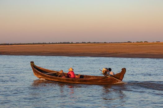 A man and two women are traveling in a wooden boat on the Irrawaddy in Myanmar