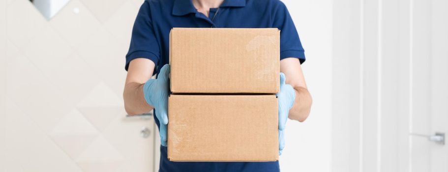 Man from delivery service in t-shirt, in protective mask and gloves giving food order and holding boxes over white background