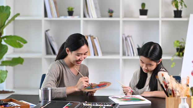 Happy young Asian mother and daughter painting together at home.