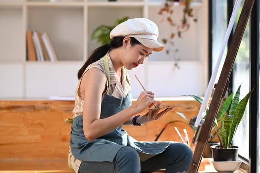 Peaceful young female artist painting picture in art studio.