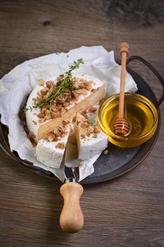 Camembert soft cheese is served on an iron dish with walnuts, honey and thyme. 