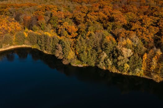 Aerial view of a blue lake next to autumn colors of a deciduous forest in Hesse