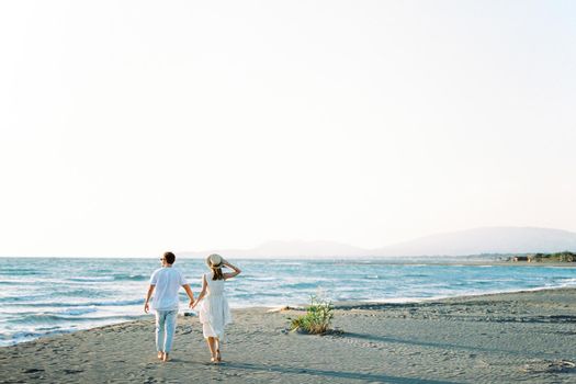 Man and woman walk holding hands on the sandy beach to the sea. Back view. High quality photo