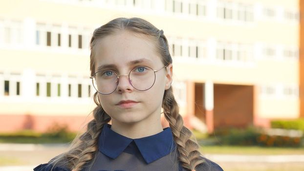 A teenage girl wearing glasses in front of a school