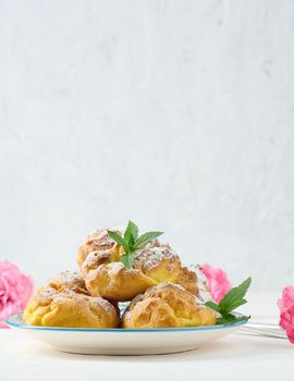 Baked eclairs with custard cream on a  round plate sprinkled with powdered sugar