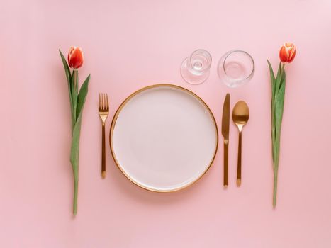 Festive pink table setting. Pink plate with gold cutlery and red tulip on pink background. Aesthetic stylish dinner table setting for Women's day, Mother's Day,wedding or anniversary.Copyspace topview