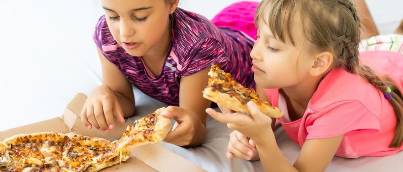 Two little girls eating pizza at home.