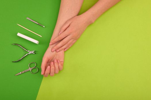 Hands with natural color manicure next to instruments for the procedure on green background