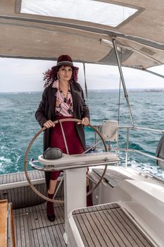 Attractive middle-aged woman at the helm of a yacht on a summer day. Luxury summer adventure, outdoor activities