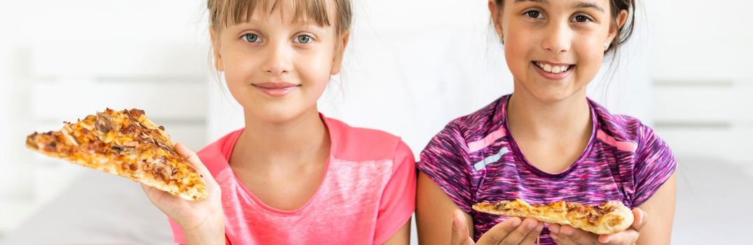 Two little girls eating pizza at home.