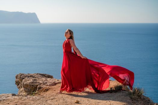 A woman in a red flying dress fluttering in the wind, against the backdrop of the sea