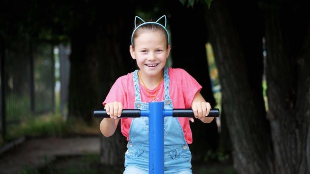 smiling, happy eight year old girl engaged, doing exercises on outdoor exercise equipment, outdoors, in the park, summer, hot day during the holidays. High quality photo