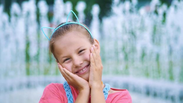 portrait of a smiling, happy eight-year-old girl in a fun hoop with ears on her head, hair ornament. on the background of fountains, summer, hot day during the holidays. High quality photo