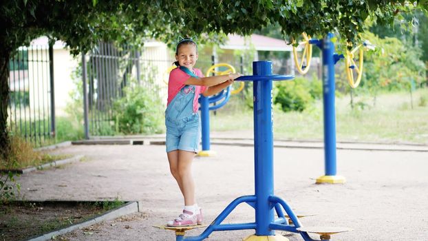 smiling, happy eight year old girl engaged, doing exercises on outdoor exercise equipment, outdoors, in the park, summer, hot day during the holidays. High quality photo