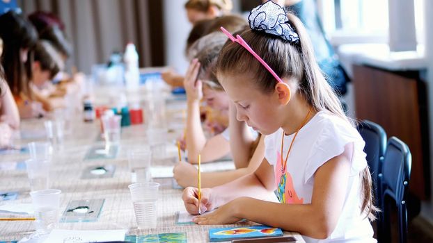 drawing lesson, in the classroom, children draw with colors, master the technique of drawing on glass. in the foreground a beautiful eight-year-old blond girl with a passion draws. High quality photo