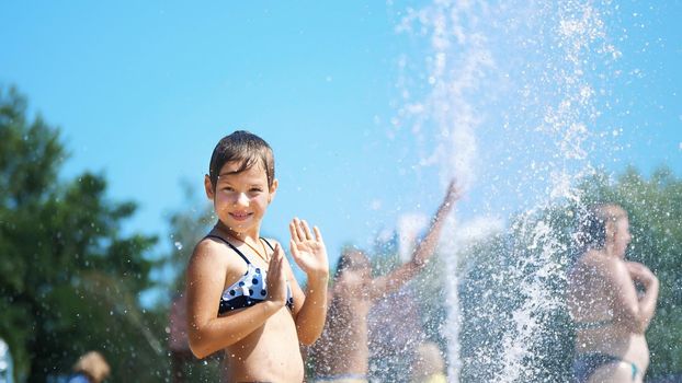 smiling, happy eight year old girl in swimsuit having fun in splashes in street city fountain, outdoors, in park, summer, hot sunny day during vacation. High quality photo