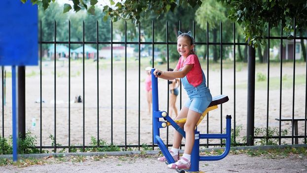 smiling, happy eight year old girl engaged, doing exercises on outdoor exercise equipment, outdoors, in the park, summer, hot day during the holidays. High quality photo