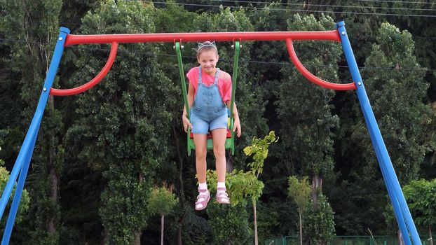 smiling, happy eight year old girl swinging on a swing, outdoors, in a park, summer, hot day during a vacation. Little girl having fun on a swing outdoor. High quality photo