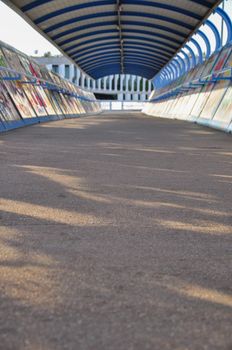 Urban covered bridge with graffiti. Sunset rays and shadows on the walkway asphalt floor in Madrid, Spain