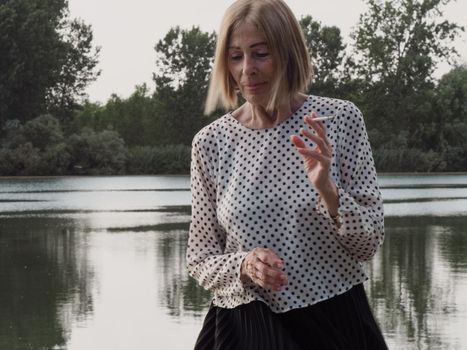 female pensioner having fun and smoking a cigarette in a park - aging free and wellness concept