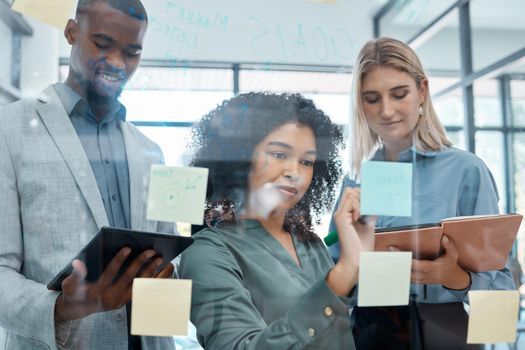 Planning, collaboration and strategy with a team working on a glass wall with stick notes in their office. Teamwork, writing and communication for the mission, vision and growth of their business.