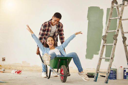 DIY, painting and happy couple smile while moving into new home, real estate property house or building. Love, creative man and woman on wheelbarrow interior design and renovation work on room wall.