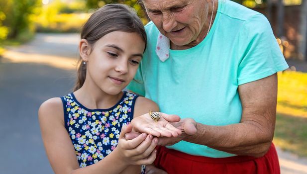 Grandmother and child are studying the snail in the park. Selective focus. Nature.