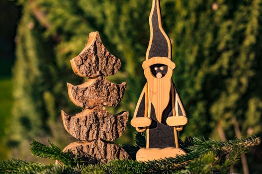 A classic wooden Santa Claus next to a wooden Christmas tree, beautifully cut out in front of a green coniferous forest
