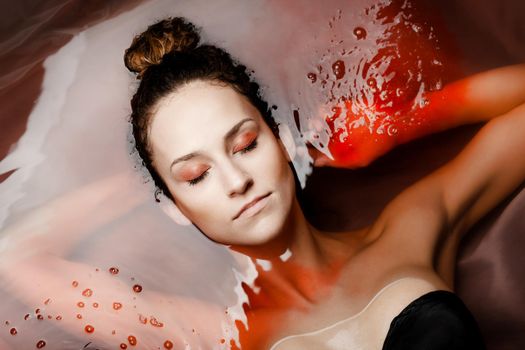 Underwater beauty portrait of a beautiful caucasian girl. Eyes closed. Red colored water.