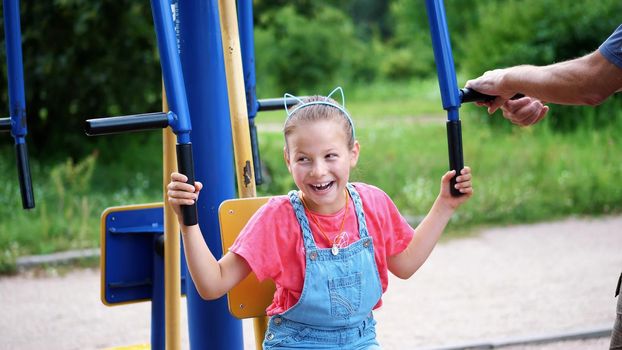 smiling, happy eight year old girl engaged, doing exercises on outdoor exercise equipment, outdoors, in the park, summer, hot day during the holidays. High quality photo