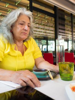 senior woman using chopsticks at the table asian restaurant outdoors