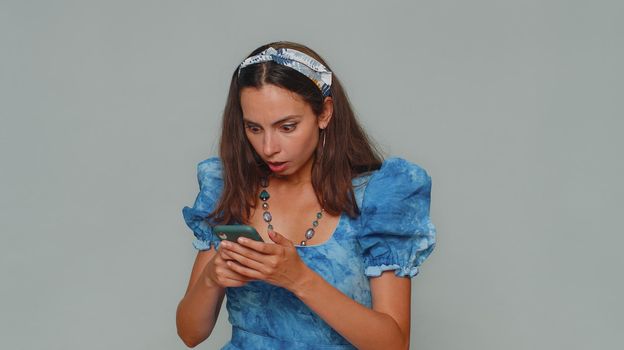 Sad young woman in blue princess dress use smartphone typing browsing, loses becoming surprised sudden lottery results, bad fortune, loss. Adult stylish girl isolated on gray studio background indoors