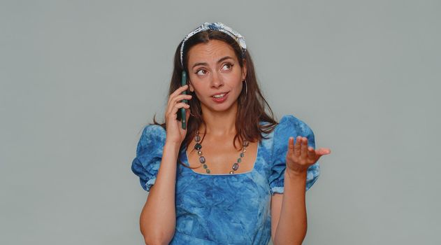 Tired sleepy freelancer young woman talking on mobile phone with friend, making online conversation. Disinterested female girl having annoyed boring talk on smartphone on gray studio wall background