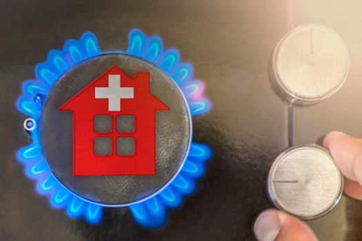 Heating season or gas use in Switzerland. Concept, model of a house stands near the flame of a gas boiler on a black background. The cost of using natural gas in Switzerland