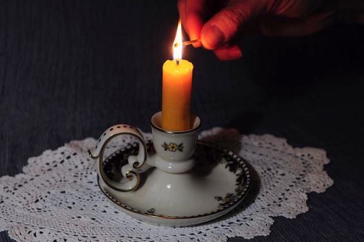 a hand lights a yellow candle in a ceramic candlestick in the dark High quality photo