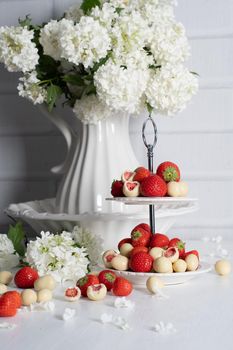 vase with white chocolate covered strawberries and fresh strawberries against porcelain vase with hydrangea, vintage still life and summer food. High quality photo