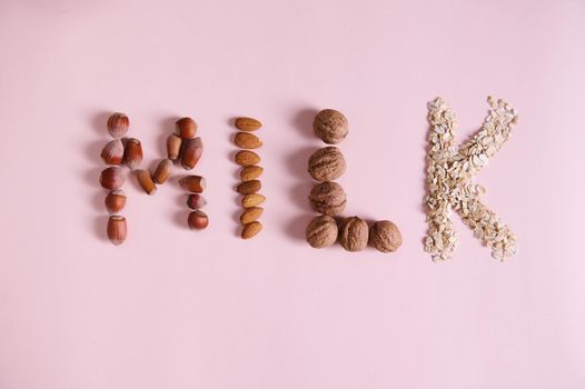 Flat lay. Lettering Milk using various healthy nuts, cereals on pink background with advertising copy space. Alternative organic raw vegan healthy drink made from oats, almonds, walnuts and hazelnuts