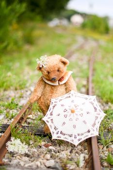 small adorable brown teddy bear sits in a copper pot on an abandoned railroad d alone, plush friend handmade, vintage and retro. High quality photo
